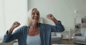 Happy excited senior woman dancing to music in home living room, celebrating achievement, singing song with toothy smile, laughing, enjoying energetic motion, active leisure, success, luck