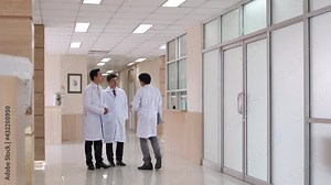 Wide shot of Hospital or healthcare lobby waiting area with group of professional doctor walking through corridor hallway and talk about patient symptoms. Hospital and medical health center concept.