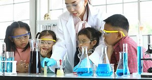 Science teacher teach Asian students, teacher pouring purple liquid to beaker and drop something into beaker, colorful test tube and microscope on table , concept for study in laboratory room.