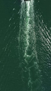 Tug boat in open calm sea, heading back to port at sunset, helps large container ships maneuver. Aerial vertical view, maritime industry, oceanic transportation or business concepts.