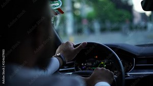 Close up view from back seat, slow motion of male driver holding hands on wheel steering automobile checking safety on road in city following traffic rules and speed limits. Blurred windshield view