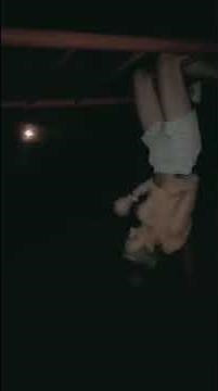 Girl is hanging from monkey bars by her legs and raises up and hits her head.