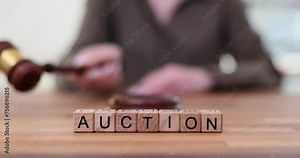 Woman with mallet takes bidding behind word Auction at desk