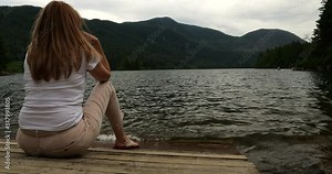 Middle aged woman sitting on the lakeside of Hicks Lake in Sasquatch Provincial Park and enjoying the lake and mountain view Stock Video