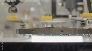 Conveyor with moving by probe arm details on automated control system with flashing scanner, people walking on background. Scanning computer-aided quality system. Automatic test set items scan on belt