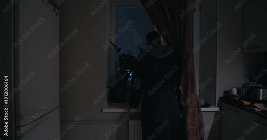 A man in a robe looks at the weather outside the window and the temperature at night