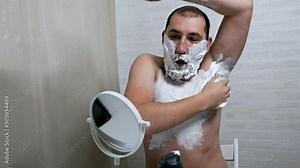 A shirtless young man puts shaving foam on his palm while preparing to shave his chest, applying shaving foam to his body and face. Hair removal on the chest and armpits, face in men
