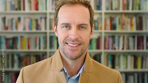 Portrait of a happy and intelligent male professor, researcher or author feeling confident with a big smile. University lecturer and literature professor standing in front of a library bookshelf
