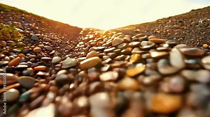 Sun is shining on a line of pebbles creating a natural border between the beach and the grass. The focus is on the pebbles in the foreground