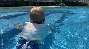 Happy little boy in swim vest life jacket for kids learning to swim in resort hotel pool in summer. Cute little child in float lifejacket swimming in outdoor pool.