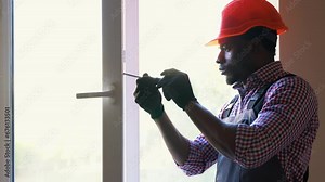 Black handyman adjusting white pvc plastic window indoors. African worker using screwdriver to repair upvc window. Homework maintenance