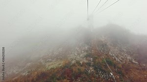 Cable car of a ski lift in a high-altitude Alpine mountain resort in autumn on a cloudy day. The chairlift ski cable car is empty. Scenic panoramic wide view of the mountain slopes in the fog