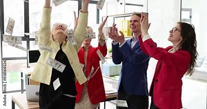 Joyful colleagues catch dollar banknotes falling from air celebrating good deal in office. Cheerful man and women have fun with money rain after successful deal slow motion