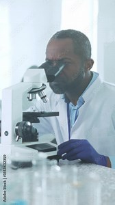 Black male scientist meticulously investigates biomedical sample using advanced microscopy techniques in lab Stock Video