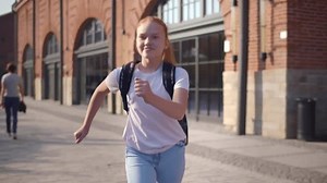 Happy teenage girl run to school. Smiling schoolgirl running outdoors after classes. High school student girl run outside school building. Back to school, education concept. Realtime.