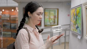 Culture and education. Portrait of smiling caucasian woman using a smartphone. Virtual excursion with audio guide in the art gallery. Slow motion. Exhibition and visit to the museum.