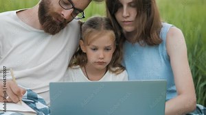 Cute family looking at laptop screen searching any information outdoors on a field.Mother, father and cute little daughter using laptop, making notes