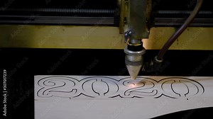 Industrial laser is cutting a pattern, numbers 2020, on a plywood sheet . Laser cutting of plywood.
