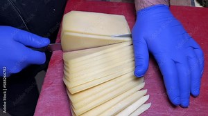 Close-up of cutting cheddar on board. Attendant slicing cheese at the deli counter
