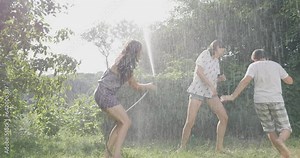 Mother and children play with water from a garden hose. A happy family rests, rejoices and splashes with water in hot summer weather. Watering in the garden near the house.