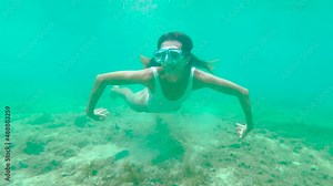 Slow motion. Young woman diving underwater in pristine clear water cenote in Mexico. Bikini girl swimming underwater in blue lagoon enjoying tropical vacations