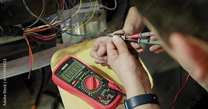 Mechanic diagnosing and repairing a car's electrical system using a multimeter. Focus on technician's hands and wires. Detailed shot in an auto service center. Car repair service. Working with cables