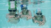 Three smiling kids enjoying underwater swim in the pool. Kids are...