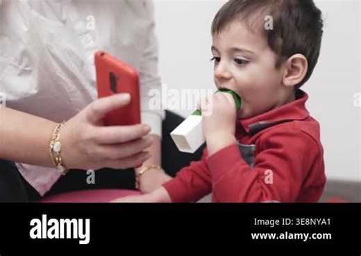 Young boy using a special vibrating teether for oral stimulation. Speech therapist holding a smartphone to distract or reward the child