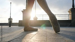 Close up of a ballet dancer's feet as she practices pointe exercises on the stone embankment. Woman's feet in pointe shoes. Ballerina shows classic ballet pas. Slow motion. Flare, gimbal shot
