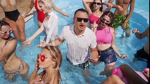 Group of friends and singers at summer pool party enjoy warm weather, sing and swim dressed and in open bikinis on holidays. Male and female going crazy, having fun, laughing loud and dancing.