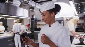 African American female chef wearing chefs whites in a restaurant kitchen using a phone and smiling | Free Stock Video Footage