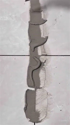 Applying gray grout to tile joints using a small scraper and wiping the excess for a clean finish