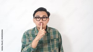 Footage of secret young Asian man in plaid shirt says hush be quiet with finger on lips shhh gesture.