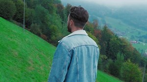 Back view of a guy walking in front of beautiful landscape with mountains and lake in Switzerland. Bearded relaxed man male walking on a nature
