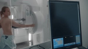 Adult woman stands topless undergoing mammography screening checkup in hospital radiology room. Computer control panel screen for activating mammogram machine. Breast cancer prevention. Modern clinic.