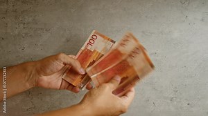 Hands holding norwegian kroner on a concrete background, showing 100 krone banknotes with a detailed close-up view of the money and fingers.