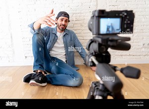 young attractive man in casual clothes hat beard hipster style with video camera on tripod against brick wall background in internet blog and blogger Stock Photo - Alamy