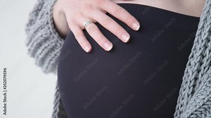 A pregnant girl in a gray jacket and black lingerie stroking and hugging a big belly. 40 weeks pregnant. Belly close-up. Expecting a baby. Slow motion. 4K