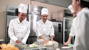 Download Multiracial professional gourmet team, four chefs in white cook uniforms and aprons knead pastry dough and eggs, prepare bread, and bakery food, baking in oven at stainless steel restaurant kitchen. for free
