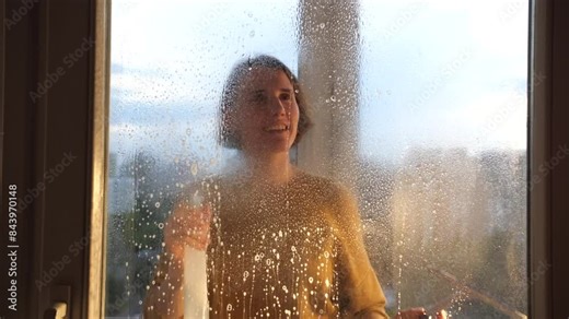 young smiling woman sprays detergent on window glass. A woman washes a window