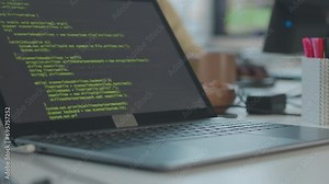 Closeup of green lines of HTML code appearing on black laptop screen at table in modern office with unrecognizable programmer working in blurred background