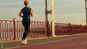 back view caucasian woman athlete running on the bridge slow motion female with blond hair trains in the early morning beautiful view on blue sky and river