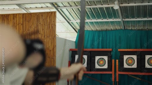 Archer releasing arrow towards target indoor