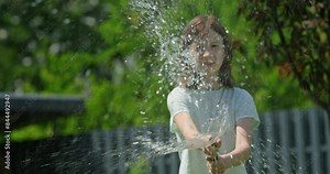 Playful girl enjoying a garden hose on a hot day.