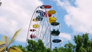 Large, multi-colored ferris wheel rotates against a blue and slightly cloudy sky. ferris wheel in an amusement park.