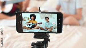 Art Bloggers, Online Lesson Recording, Woman Blogger, Playing Guitar. Cheerful kids bloggers are recording guitar lessons on a smartphone. Smartphone screen