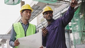 Structural engineers and construction workers are holding blueprints inspecting structure. sky train track construction in city. Blue collar wears a safety hardhat while working on construction site.