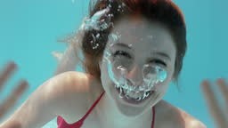 beautiful woman swimming underwater in pool smiling waving hand...