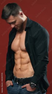 Muscular young man in studio. Strong muscular bodybuilder man with perfect trained body standing against background Vertical video