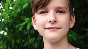 a ten-year-old boy looks into the camera against the background of green leaves of a bush.